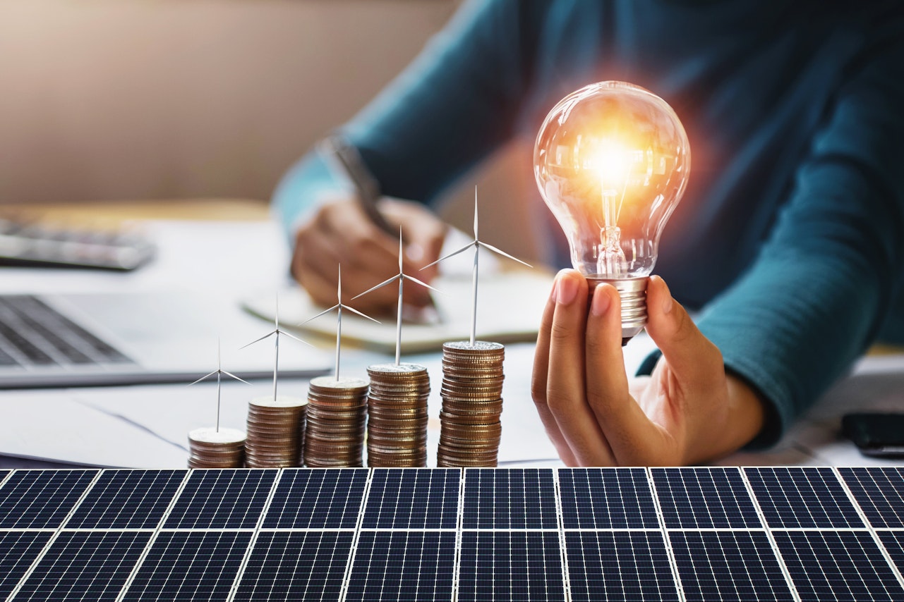 businesswoman-holding-light-bulb-with-turbine-coins-solar-panel-concept-saving-energy-finance-accounting